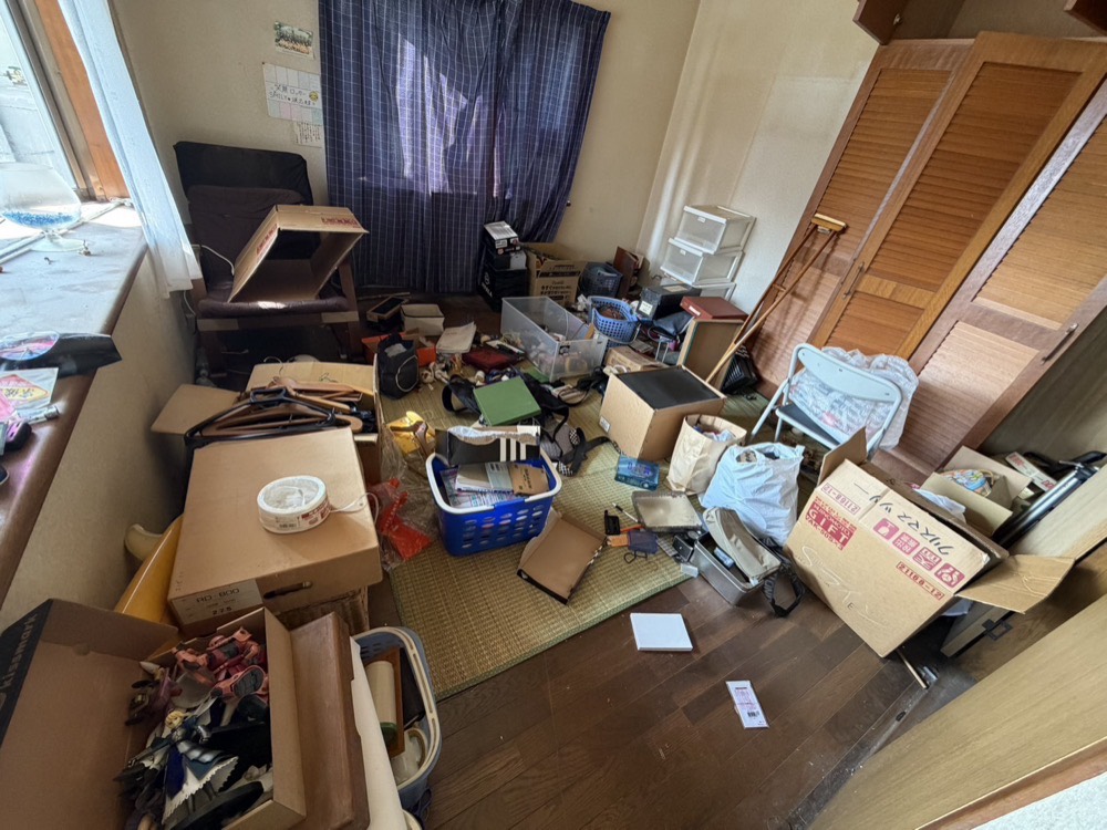 居室の片づけ前。家具や荷物が部屋いっぱいに残された状態